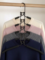 A black metal multi-hanger garment organizer hanging on a wooden rod, holding four nested crewneck sweaters in cream, pink, gray, and navy blue.
