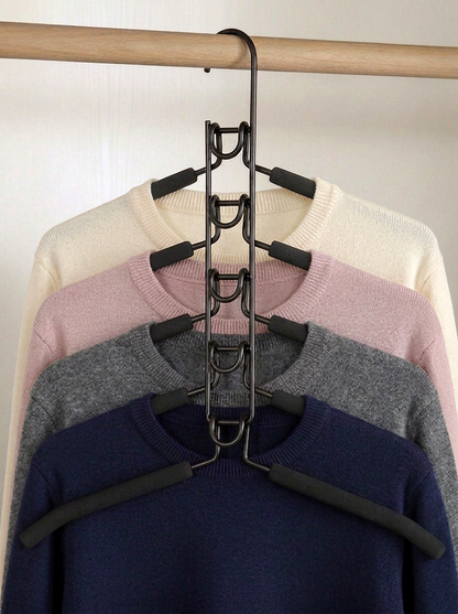 A black metal multi-hanger garment organizer hanging on a wooden rod, holding four nested crewneck sweaters in cream, pink, gray, and navy blue.